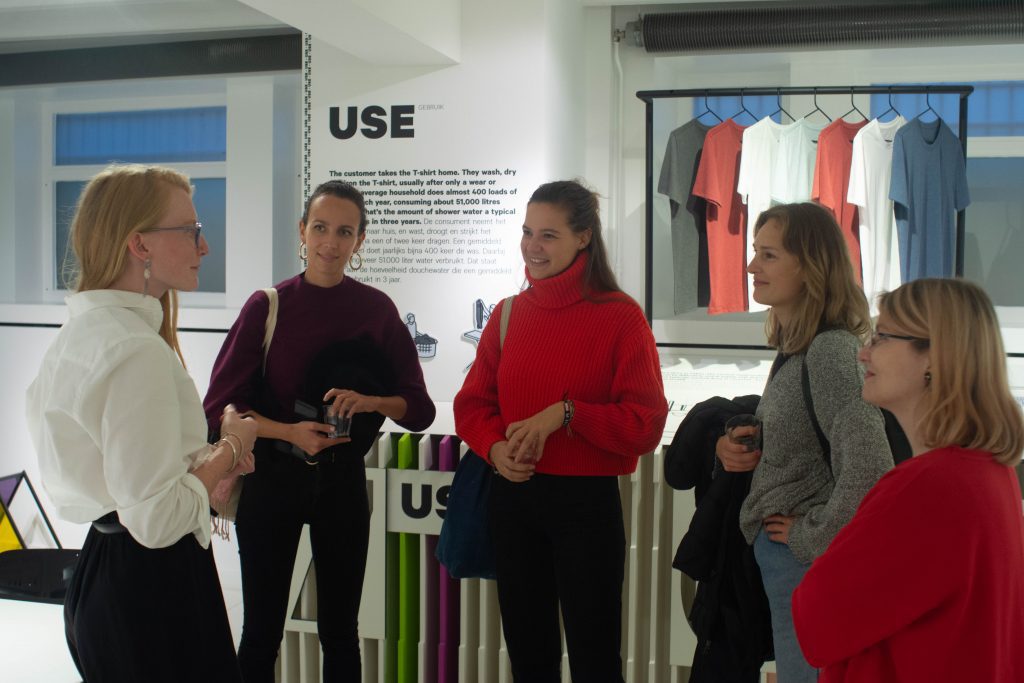 The basement of the Fashion for Good Museum displays and explains the production cycle of T-shirts. These women eagerly listen to a Fashion for Good tour guide explain the goals of the museum. 